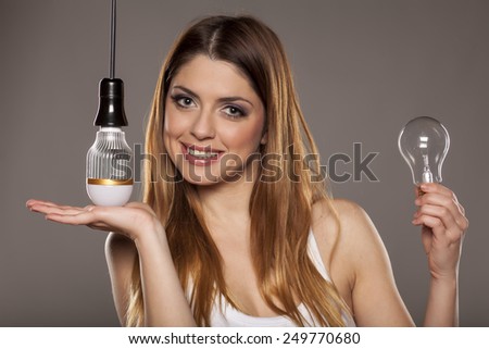 young smiling woman holding an old tungsten and new LED bulbs