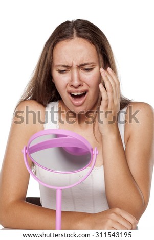 unhappy young woman without make-up touching her face in the mirror