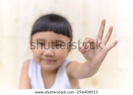 Kid with hand ok symbol and blur face on wood wall background