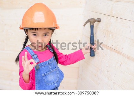 Little girl on carpenter jobs hammer on wood wall and ok sign