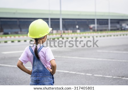 Little girl with green helmet in warehouse center background; Transportation work
