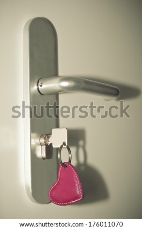 Key with red heart key chain in keyhole wooden door. soft focus