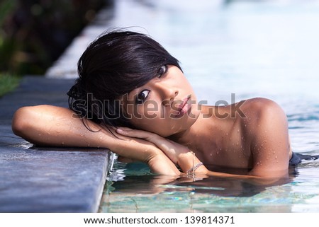 young girl sitting in the pool, leaning on one of the sides and tilted her head to one side