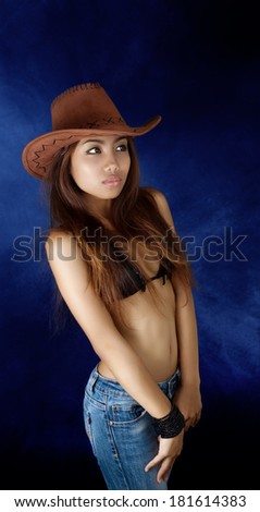 Cowgirl in jeans and a bikini and cowboy hat, studio performance on black and blue background of muslin