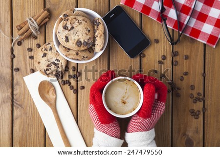 Hands in gloves holding hot cup of coffee and chocolate cookies