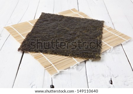 A sheet of dried seaweed Nori on a makisu mat on a white aged table