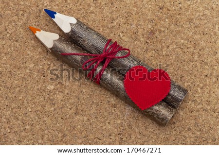 Photography with a gift on Valentine\'s Day. Textile red heart, two wooden pencil related red cord on a cork background. Can be used as greeting card for Valentine\'s day.