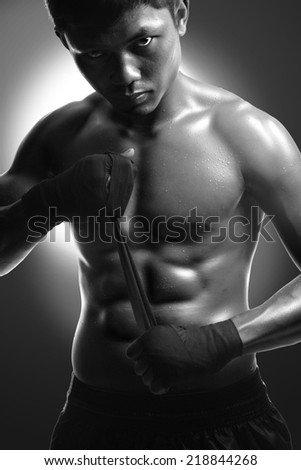 Young male boxer wrapping his hands in boxing tape before a fight.