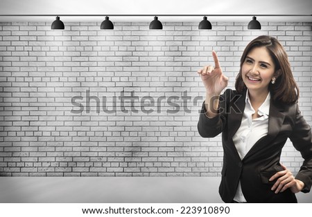 Business Woman touching an imaginary screen with her finger. on brick wall background with copy space for your design.