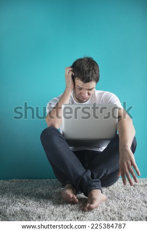 young man in t-shirt sitting at home, working on laptop computer