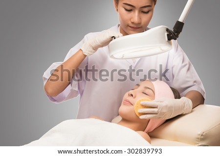 Young beautiful woman receiving cosmetic facial mask in spa beauty salon and relax. Peaceful brunette getting micro dermabrasion from beauty therapist in the health spa