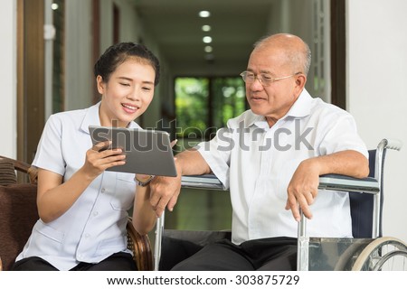 Female nurse discussing over digital tablet with senior man in wheelchair  at nursing home