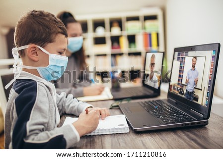 Boy and girl studies at home, wear protective masks, and doing school homework. Distance learning online education.