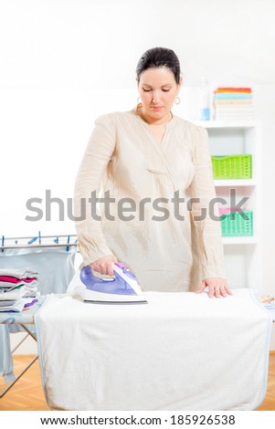 Cheerful housewife standing at the ironing board ironing clothes
