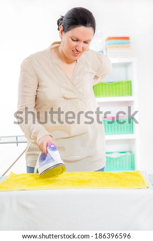 Cheerful housewife standing at the ironing board ironing clothes