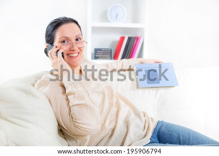 A young woman lying on the sofa reading book and use the phone