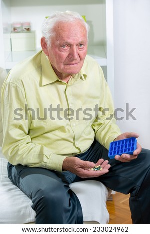 Senior man uses a pill organizer to prepare his medication for the week.