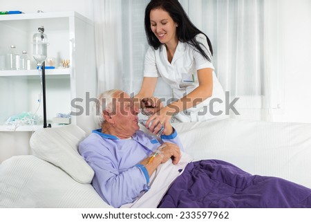 Nurse helping a man in bed to drink water