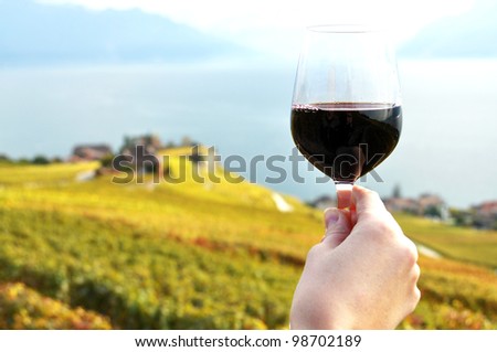 Glass of red wine in the hand against vineyards in Lavaux region, Switzerland