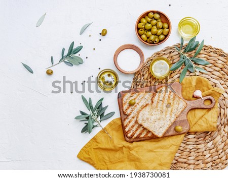 Top view organic olive oil, olives, fresh toast bread and olive branch on white background, space for text, flat lay