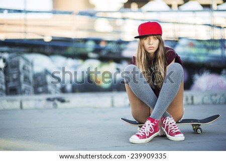 Portrait of beautiful teen girl sitting on skateboard over wall with abstract graffiti art. Urban outdoors, teenager\'s lifestyle