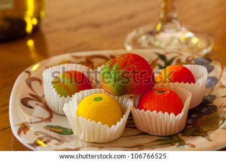 Fruit shaped candies in macro image of marzipan sweets on table with glass and bottle of wine