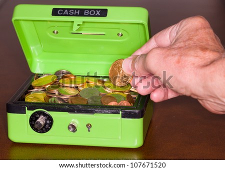 Green cash box with combination lock open to show piles of coins including gold and silver