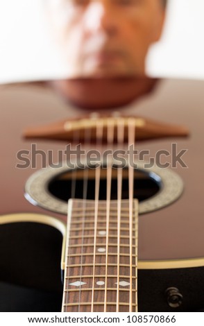 Macro shot down the fretboard of acoustic guitar with shallow depth of field with guitarist face in the distance reflected