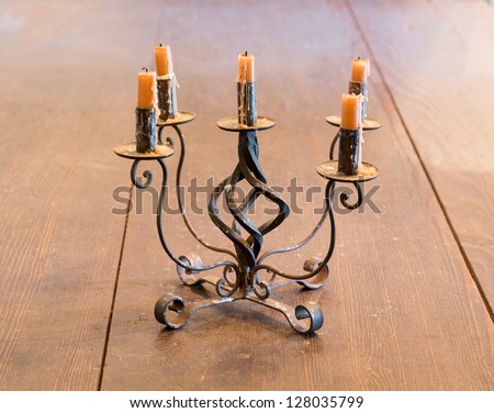 Old iron candlestick holder and candles lit by light from window on old wooden table