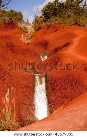 Water running in a stream down the bright red dirt of Waimea Canyon in Kauai