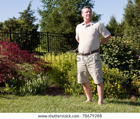 Baby boomer sitting on the grass lawn and digging for weeds in a flowerbed