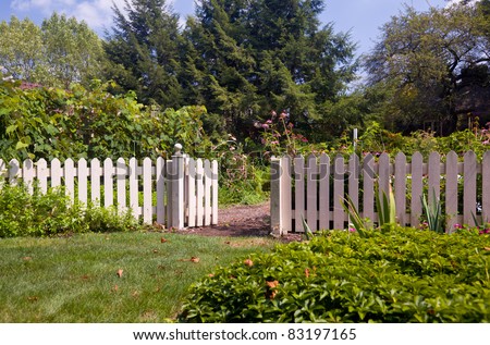 White picket fence and gate frame the entrance to a kitchen garden overflowing with produce