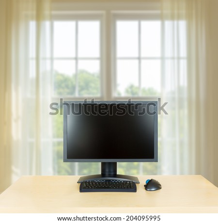 Plain light colored wooden desk with computer monitor and keyboard to suggest calm, organization and meditation at work or in home office. Bright window in background