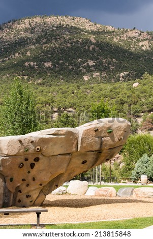 Climbing wall with hand holds and bolted fasteners with real mountain and rocks in the background