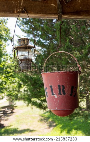 Old worn fire bucket and oil lamp hanging from rafters of log cabin