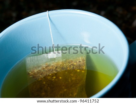 Macro of a green tea teabag brewing in hot water in a blue mug on kitchen worktop
