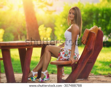 Beautiful sexy women resting in the park on a bench, sunset in the background, with color filters, and some fine film grain added