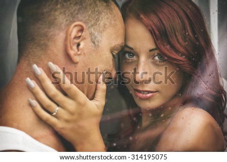 Attractive couple behind a window with water drops, in a rainy day. With custom white balance and color filters