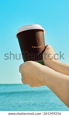 Woman hands handling paper coffee cup near the blue sea