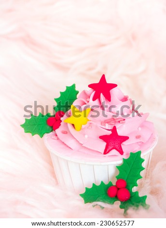 Sweet pink cupcake with stars and holly berry decorated on soft fur background