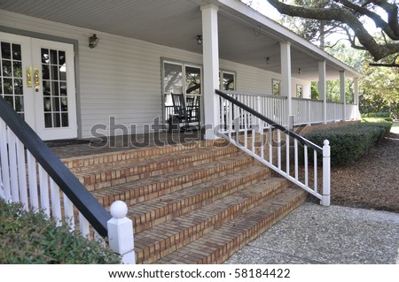 Red brick steps, with a white wooden railing, leading to a large outdoor covered porch.