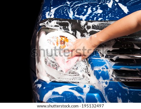 man washing a soapy blue car with a pink sponge.