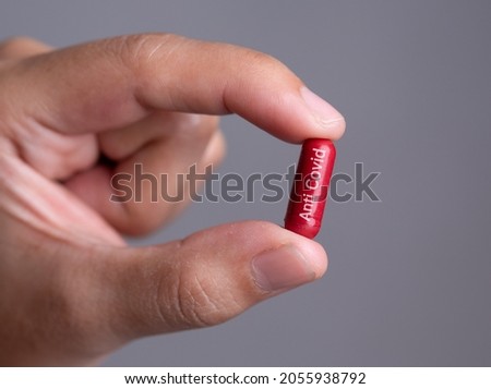Male hand holding a medical red capsule pill between fingers against gray background,Coronavirus,Covid-19 Cure,Anti-Covid 19,anti flu drug pill Stock fotó © 