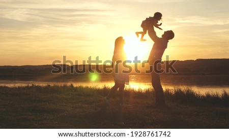 Child in the hands of parents jumps from dad to mom and laughs. Happy family walk on the beach at sunset. Child, daughter, mom, dad play fun in park in park in sun. Family fantasies, childhood dreams.