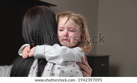 Child is crying in room in the arms of his mother. A loving young mother hugs and comforts her little daughter. Mom calms child. Family mother and baby with tears in their eyes emotionally embrace
