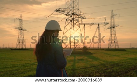 An electrical engineer, woman working with computer tablet, works with electricity next to an electric tower. Industry of energy business technologies. An electrical engineer works on digital tablet