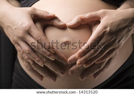 Close-up of a belly with the hands of the happy future parents making a heart shape