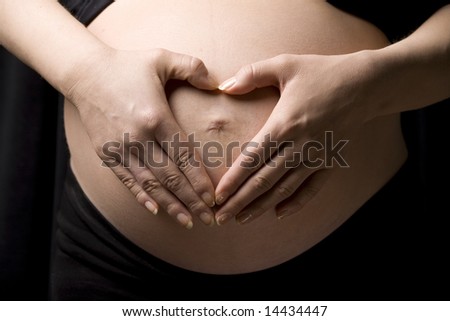 Close-up of a belly with the hands of the happy future mother making a heart shape . Happy mother