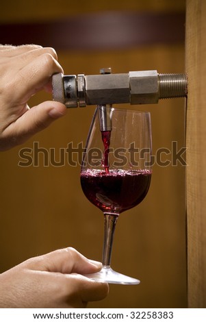 A man in a bid winery pouring vintagewine in a wineglass in order to taste how good it is. Pouring wine to taste
