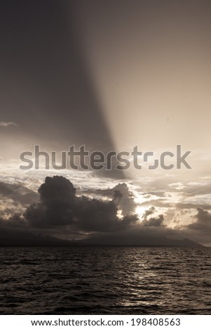 Late day sunlight passes around a low set of clouds near the island of Guadalcanal in the Solomon Islands. This tropical country is home to beautiful, diverse coral reefs.